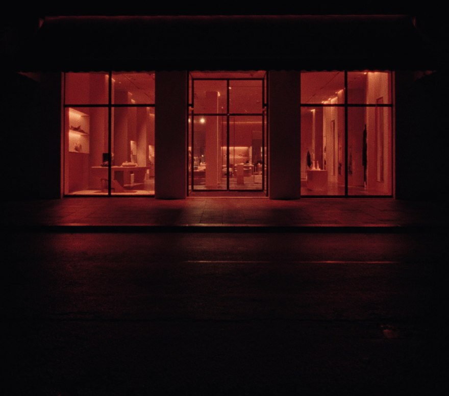 An immaculate, brightly lit shopfront at night, its windows glowing onto a completely empty street with nobody outside it.